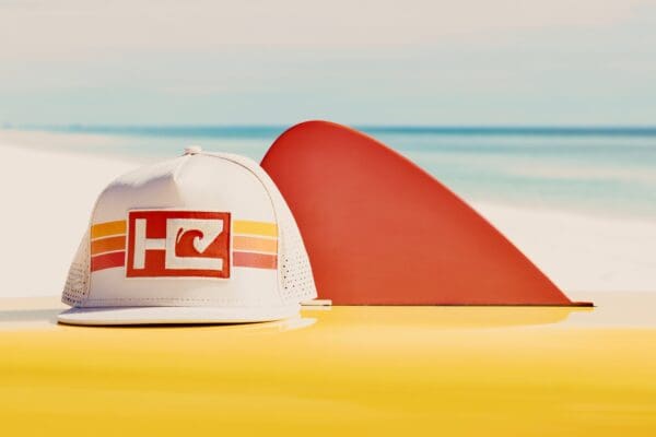White hat, red surfboard fin, beach.