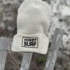 Beige Howzit Surf beanie on fence.